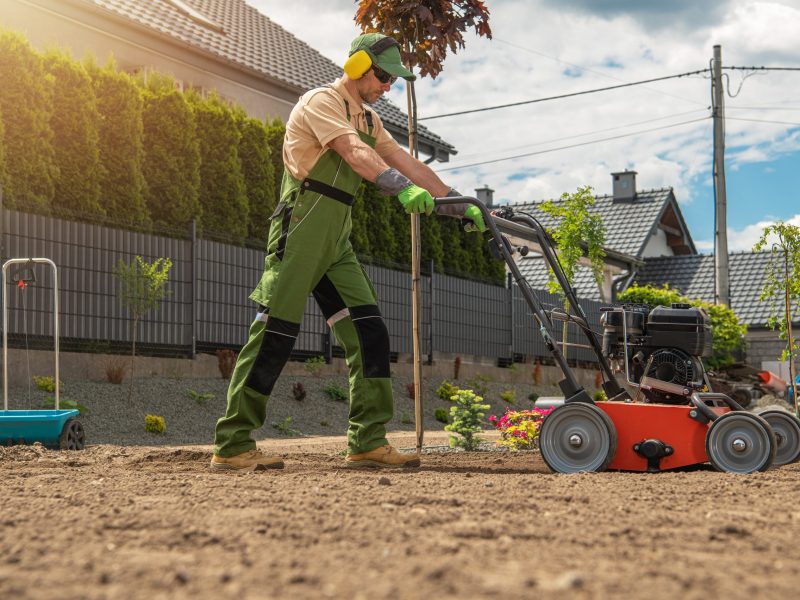 Gardener with Gasoline Engine Aerator Working Hard in the Backyard Garden. Landscaping and Gardening Theme.